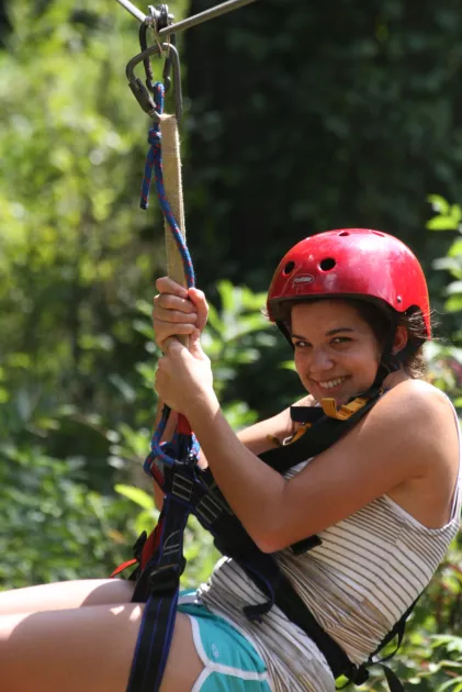 A young girl ziplining through green trees